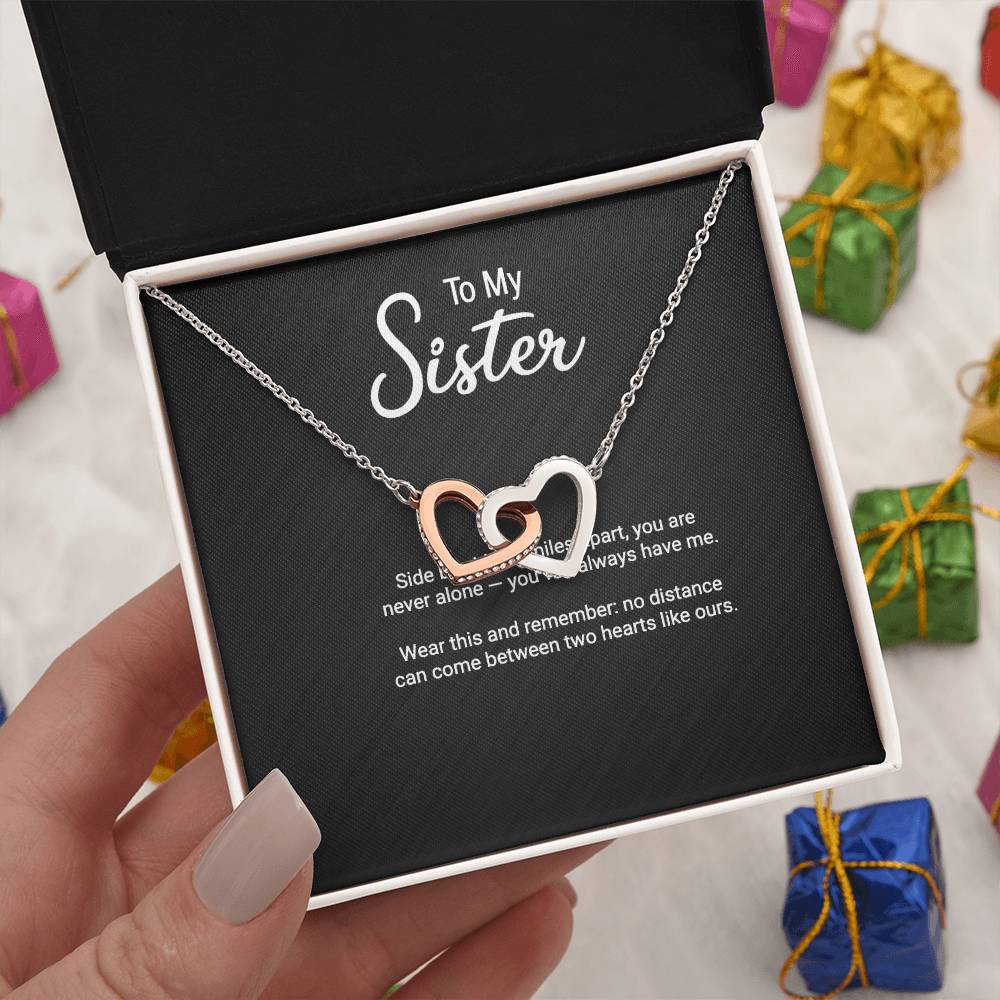 To My Sister interlocking hearts necklace with 'Side by Side or Miles Apart' message card, held in hand